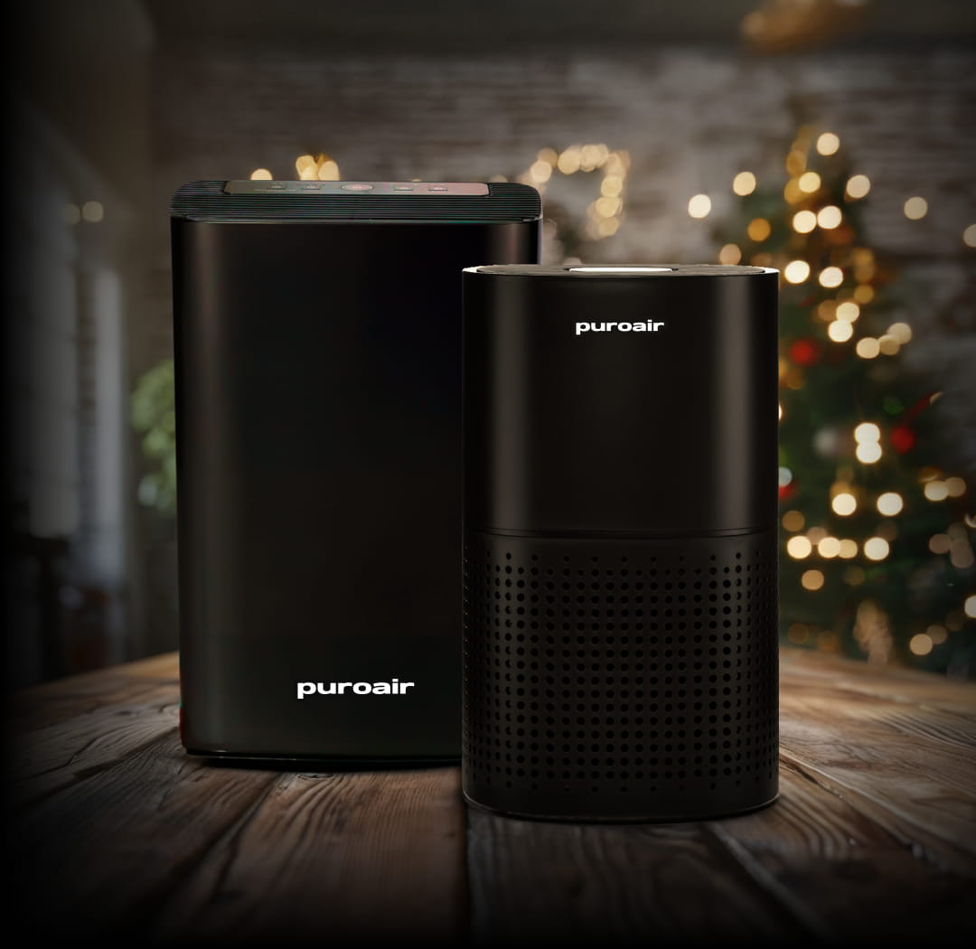 Two PuroAir air purifiers on a wooden surface with a blurred festive background