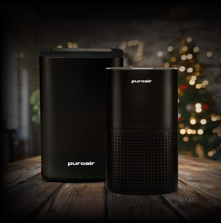 Two PuroAir air purifiers on a wooden surface with a blurred festive background