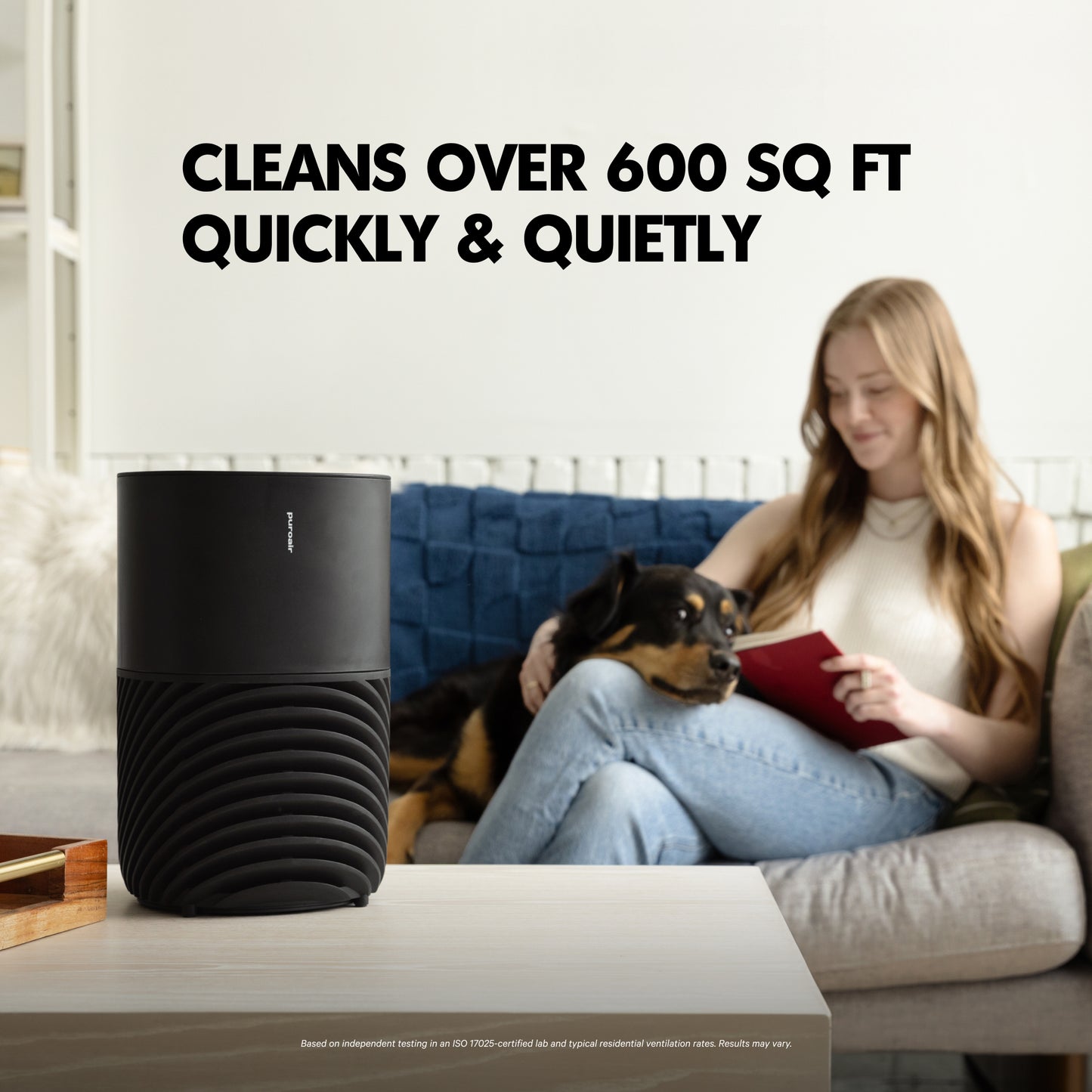 Woman sitting on a couch with a dog, reading a book, next to PuroAir 130i air purifier