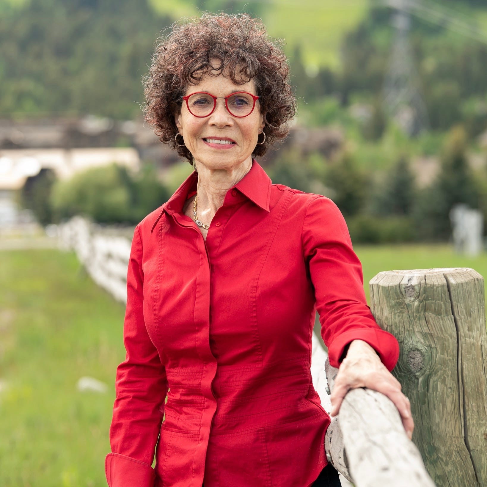 woman standing by fence wearing red shirt and red glasses