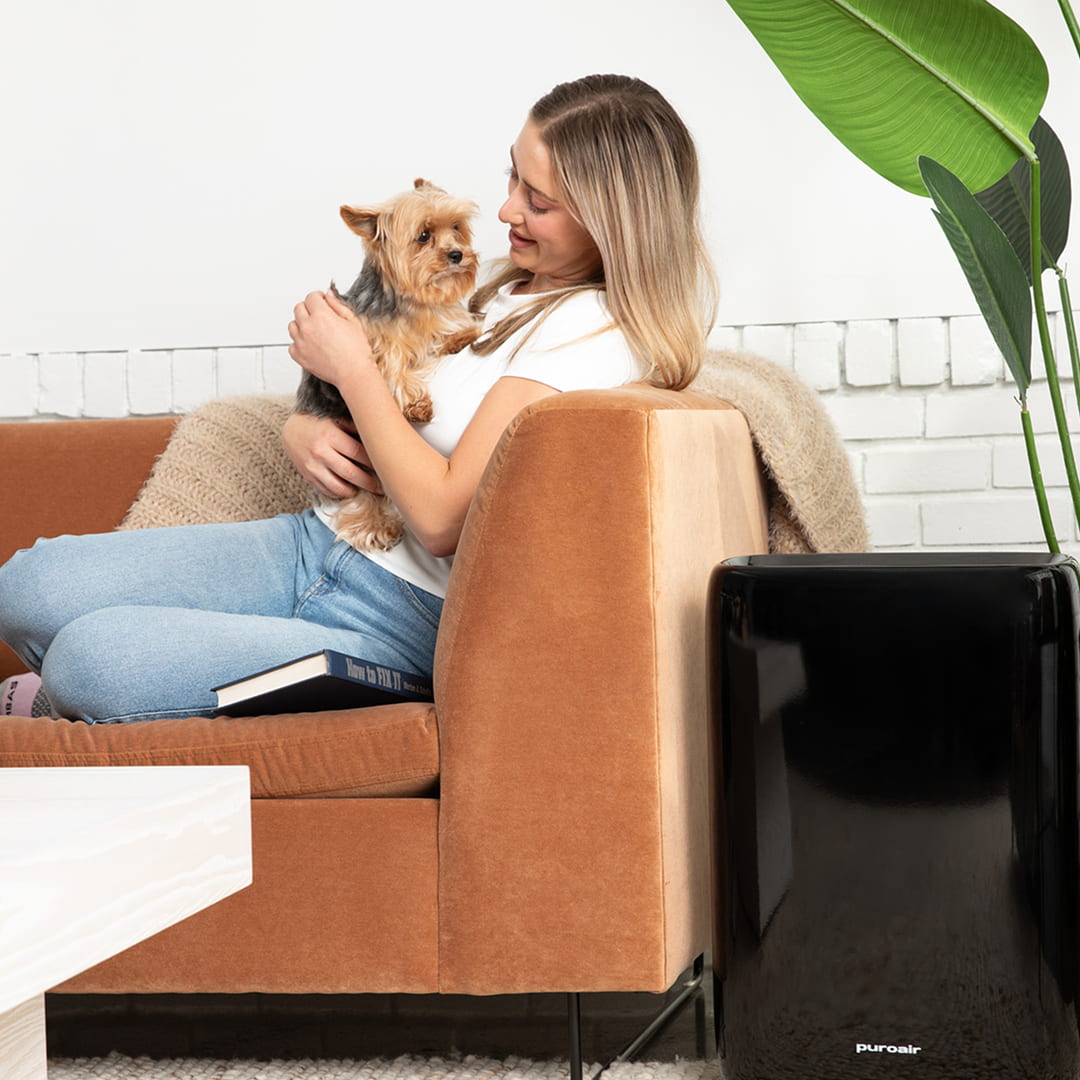 Woman sitting on brown couch holding a small dog with PuroAir 400 on ground